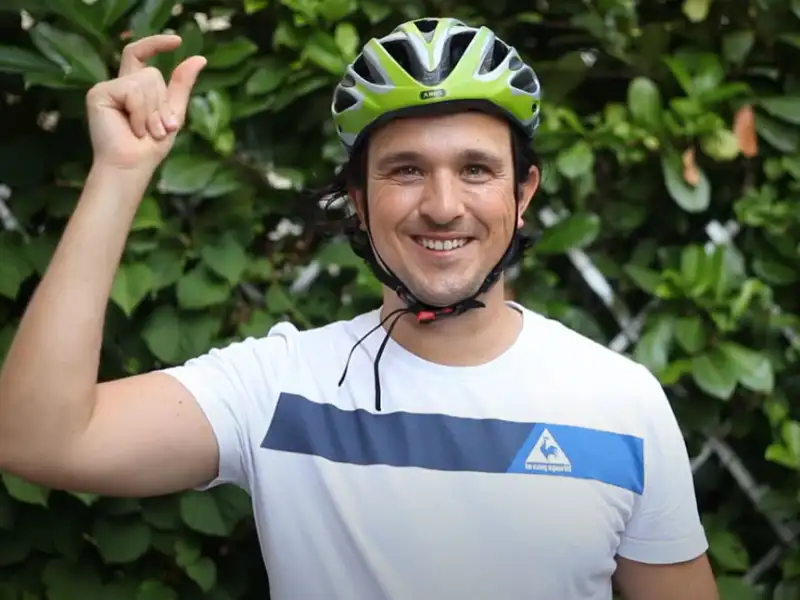 Ein American Express Mitarbeiter mit grünem Fahrradhelm vor einer grünen Hecke