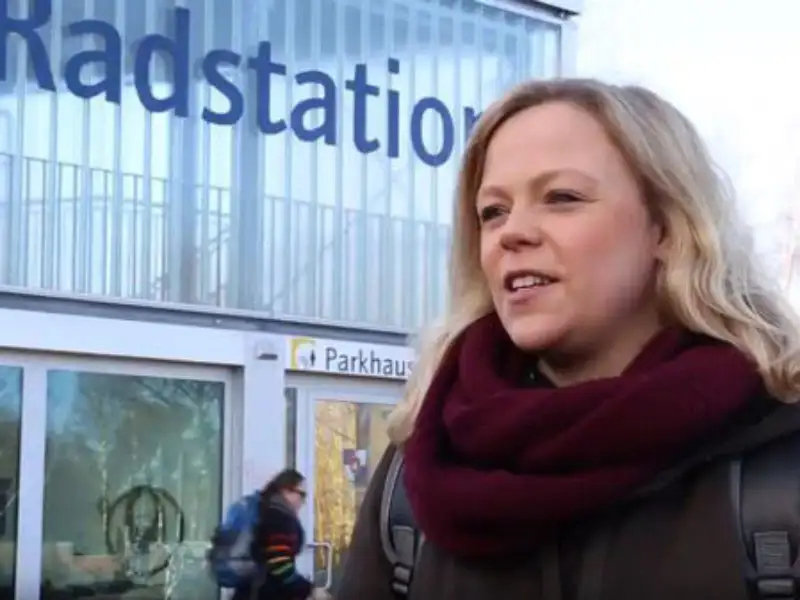 Maraike Kahlstorf von Rewe steht vor einem Gebäude mit der Aufschrift "Radstation". Sie trägt einen roten Wollschal