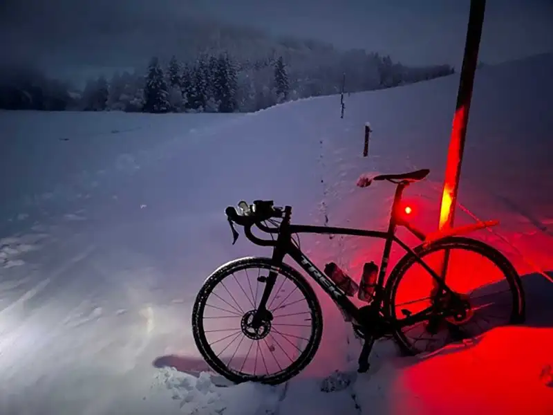 Ein Mountainbike auf verschneitem Feldweg, in der Dämmerung leuchtet das Rücklicht rot auf dem Schnee Ein Mountainbike auf verschneitem Feldweg, in der Dämmerung leuchtet das Rücklicht rot auf dem Schnee