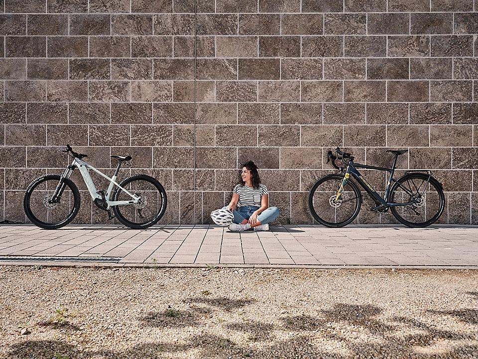 Eine Frau sitzt vor einer Mauer zwischen zwei Fahrrädern